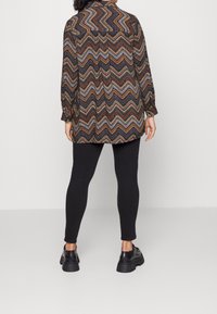 Langærmet skjorte i et flerfarvet zigzag-mønster, parret med sorte leggings og kraftige sorte sko. Har en krave og en afslappet pasform.
