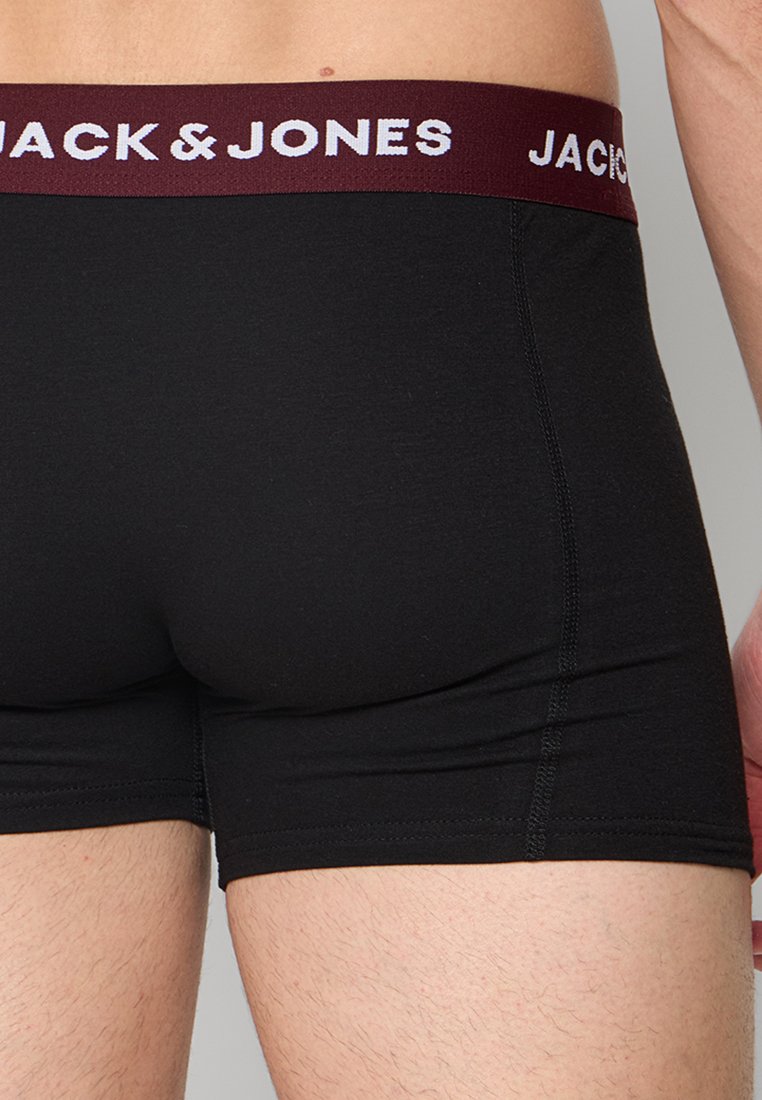 Primer plano de la parte baja de la espalda y la parte superior de las piernas de una persona que lleva bóxers ajustados negros con una cintura burdeos etiquetada como "JACK & JONES."