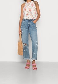 Blommig halternacke, lätt tyg; slitna ljusblå jeans med vita färgsplatter; vävd beigeväska; rosa flätade klacksandaler.