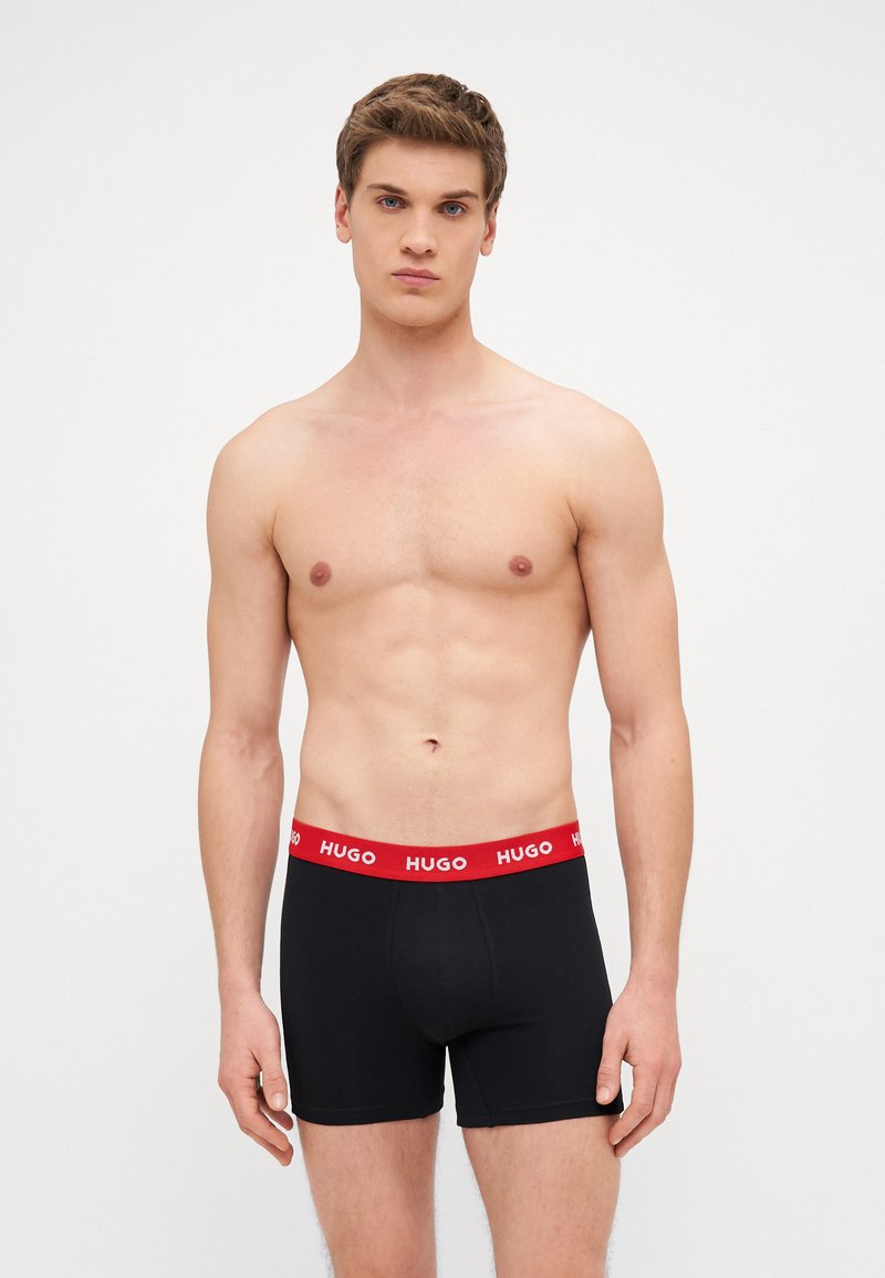 Čierne boxerky s červeným pásom s logom HUGO. Tkanina je hladká a priliehavá, s klasickým strihom krátkych nohavíc.