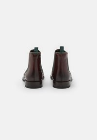 Botas de cuero marrón hasta el tobillo con paneles laterales elásticos verdes, silueta ajustada y tacón apilado. Incluyen lengüetas para facilitar el calzado.