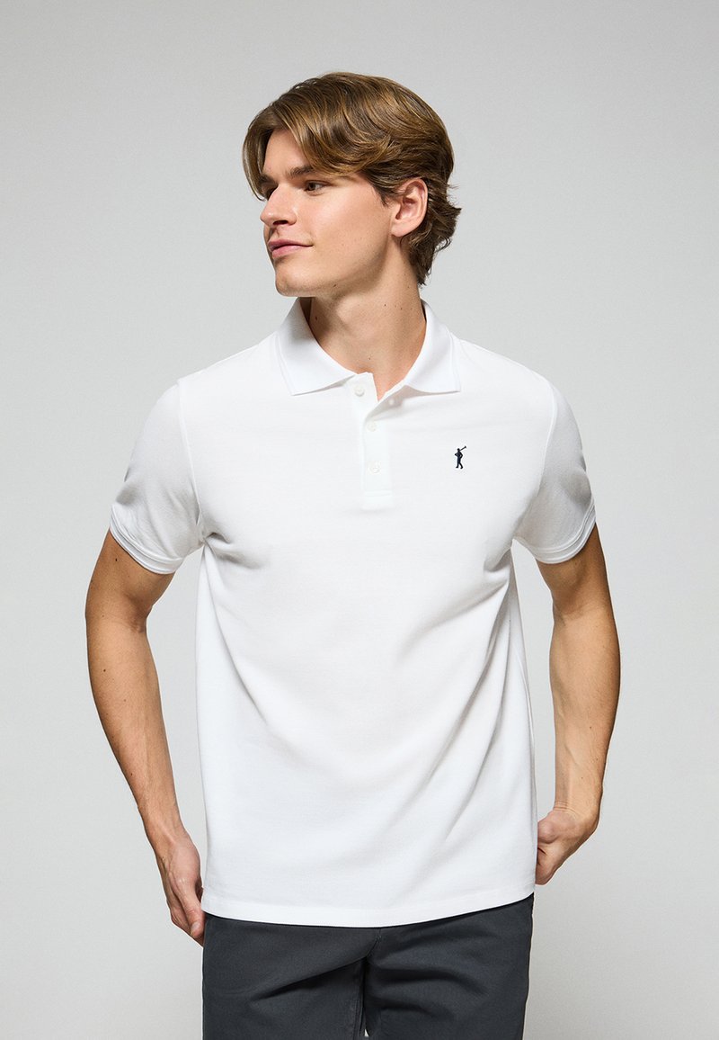 Polo bianco a manica corta in cotone con collo a tre bottoni e un piccolo logo blu marino sul petto. Texture liscia e design aderente.