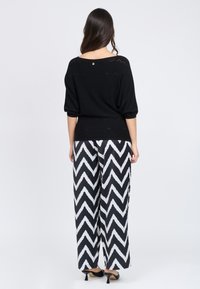 Maglia nera oversize a maglia con dettagli a zigzag, abbinata a pantaloni a gamba larga bianchi e neri con motivo a zigzag e tacchi neri.