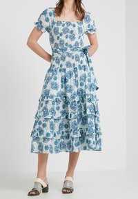 Blå och vit blommig midiklänning med puffärmar, lager med volanger och en åtsittande liv. I kombination med flerfärgade klumpiga sandaler.