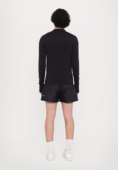 Schwarzes Langarmshirt und schwarze Shorts, beide in einem figurbetonten Design. Die Shorts sind leicht und haben ein Logo auf der linken unteren Seite.