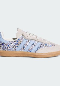 Hellblaue und beige Sneaker mit Blumenmustern, drei blauen Streifen und einer strukturierten Gummisohle. Weiches Wildleder- und Stoffmaterial.
