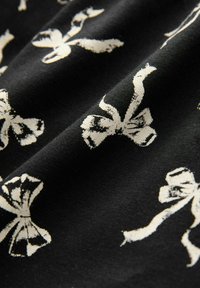 Black fabric featuring a repeated pattern of white bows, with a soft texture and subtle sheen, creating a delicate visual effect.