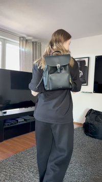 Zwarte leren rugzak met een klep, voorvak met ritssluiting en verstelbare schouderbanden. Glad oppervlak, minimalistisch ontwerp en zilveren hardware accenten.