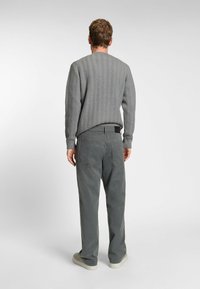 Szary sweter dziany z teksturowanym wzorem w jodełkę, w połączeniu z szarymi spodniami o wysokim stanie. Buty są w jasnym kolorze, z zaokrąglonym czubkiem.