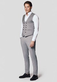 Jasnoszary garnitur trzyczęściowy z podwójnym zapięciem kamizelki, czarnymi guzikami i dopasowanymi spodniami. W połączeniu z białą koszulą i czarnymi butami.