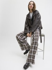 Braune Leder-Motorradjacke, graues T-Shirt, karierte weite Hose in Braun und Creme sowie klobige schwarze Plateau-Stiefel.