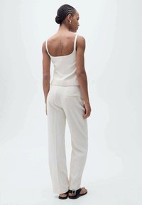 Lichtbeige mouwloze top en bijpassende broek met hoge taille, met een gladde textuur, minimalistisch design en twee achterzakken.