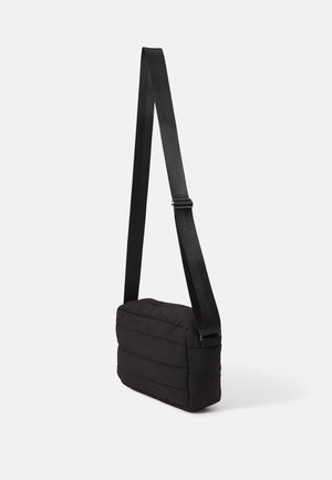 Czarna, pikowana prostokątna torba na ramię z regulowanym długim paskiem, przedstawiona na jednolitym jasnym tle.