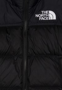 Black puffer jacket with central zipper and white embroidered "THE NORTH FACE" logo on the upper left side.