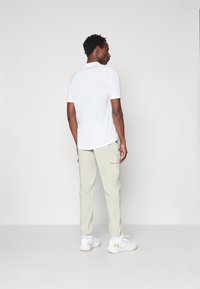 T-shirt de sport blanc à manches courtes, associé à un pantalon cargo beige clair avec des poches latérales, et des chaussures de sport blanches.