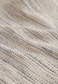 Beige woven fabric with a grid pattern, featuring textured strands and subtle dark accents, creating a varied surface.