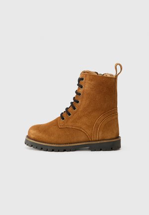Stivale alla caviglia in suede marrone con lacci neri, suola in gomma e linguetta laterale. Presenta cuciture rinforzate e un design a punta rotonda.