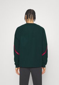 Mörkgrön sweatshirt med långa ärmar, med en rosa detalj längs sidan. Mjuk textur och rundad halsdesign.