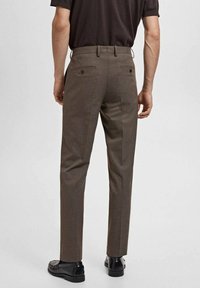 Brown dress pants with a smooth texture, slim fit design, and two back pockets secured with dark buttons, paired with black shoes.