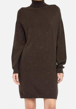 Vestido jersey de cuello alto de manga larga en marrón oscuro con un patrón moteado, llevado por una persona con manos y piernas descubiertas.