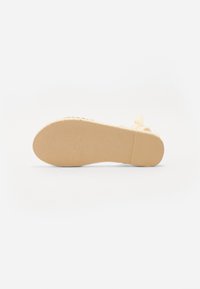 Semelle de chaussure beige avec caoutchouc texturé pour l'adhérence, possède des bords lisses et une légère courbure. Pas d'ornements ou motifs visibles.