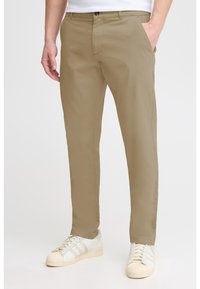 Chinos en coton beige avec une coupe à plat, poches latérales et détails de couture subtils, assortis à des baskets blanches avec des accents gris.