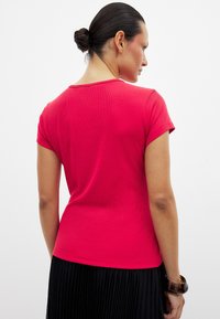 Raudonas, glamžytas trumpomis rankovėmis viršus su apvalia iškirpte, prisitaikantis prie kūno forma ir lygiu paviršiumi. Nugaros dalyje yra šiek tiek išlenkimas.