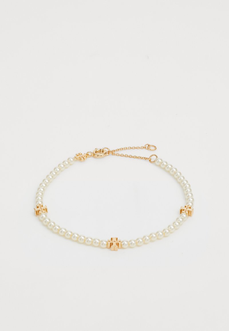 Náramek z perel s dvojitou vrstvou bílých perel, s akcenty z pozlaceného kovu na několika místech a s bezpečným zapínáním.