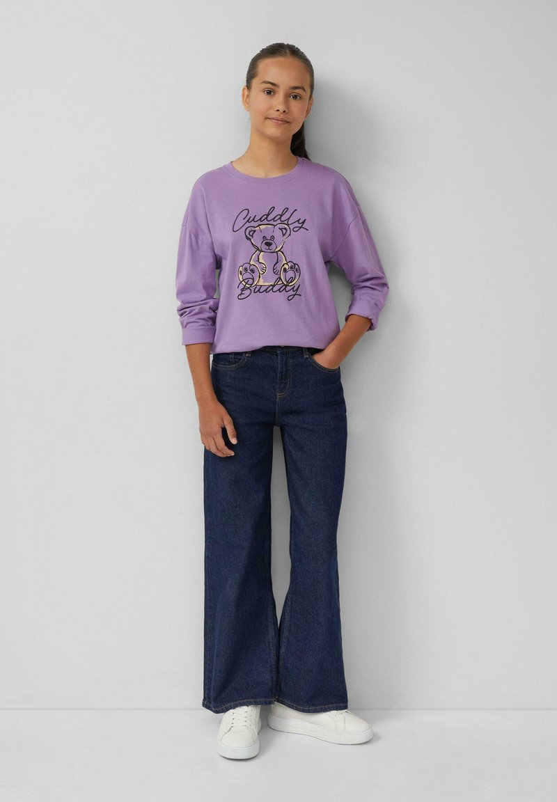 Lila sweatshirt met de opdruk "Cuddly Buddy" met daarop een beer, gecombineerd met donkere wijde jeans en witte sneakers. Gladde textuur, casual stijl.