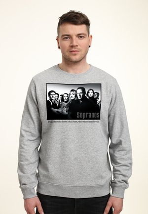 Mężczyzna w szarej bluzie z czarno-białym zdjęciem grupowym z serialu The Sopranos i napisem „Jeśli jedna rodzina go nie zabije, zrobi to druga.”