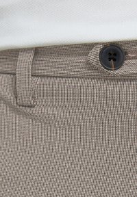 Brązowa tkanina w kratkę o gładkiej fakturze, z pojedynczym czarnym guzikiem i szlufkami na pasku w talii.