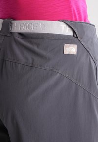 Grå byxor i lättmaterial, med en texturerad midjeband som har "The North Face"-logotyp och diagonala sömdetaljer.