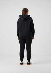 Felpa nera con cappuccio e pantaloni della tuta abbinati, caratterizzati da una vestibilità comoda, una texture morbida e polsini a coste. Sneakers con un design nero e beige.