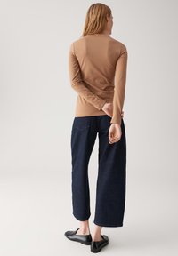 Bruine lange mouwtop met een nauwsluitend ontwerp, gecombineerd met donkerblauwe wijde denim jeans, voorzien van achterzakken en een ontspannen silhouet.