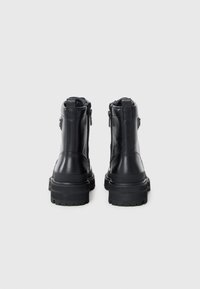 Bottes noires en cuir à chevilles avec une semelle épaisse, des fermetures éclair sur les côtés et des accents texturés. Talon renforcé pour la durabilité et le soutien.
