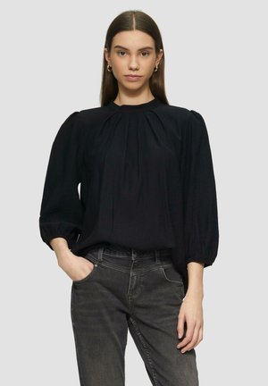 Zwarte blouse met driekwart pofmouwen, geplooide voorkant en hoge halslijn. De stof lijkt lichtgewicht en lichtjes textuur te hebben.