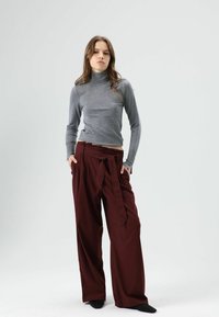 Grijze coltrui gecombineerd met bordeauxrode, wijde broek met hoge taille en een strik aan de voorkant. Zachte stof en een losse pasvorm.