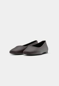 Um par de sapatos bailarina castanho-escuro, de colocar, com bico arredondado e costura mínima, sobre um fundo branco simples.