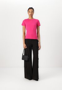 T-shirt fuchsia à manches courtes avec un col rond, associé à un pantalon large noir et un petit sac à main noir. Design simple et ajusté.