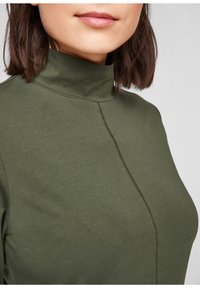 Olijfgroene top met hoge hals, gemaakt van een gladde, rekbare stof. De top heeft een subtiele naad aan de voorkant en een aansluitend ontwerp.