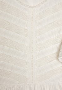 Bijela haljina s teksturiranim prugama, čipkastim detaljima niz sredinu, oštrim rubovima i napuhanim rukavima s izrezima.