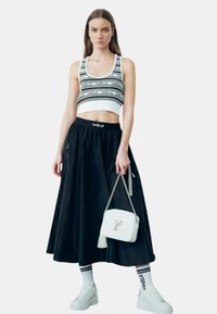 Top corto con motivo a righe bianche e nere, gonna nera a vita alta, sneakers bianche e una borsa bianca con tracolla a catena.