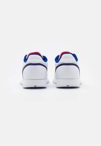 Pair of white sneakers with blue and red interior lining viewed from the back on a plain white background.