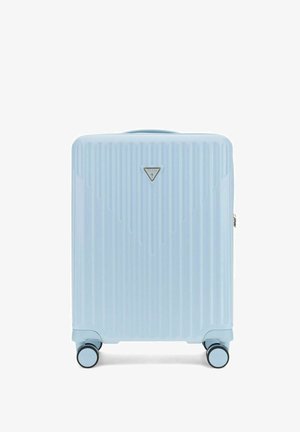 Valise rigide bleu clair avec des rainures verticales, quatre roues pivotantes et un petit logo triangulaire Guess à l'avant.