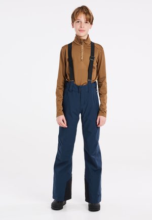 Maglia marrone a maniche lunghe con colletto piccolo e zip, abbinata a pantaloni da neve blu navy con bretelle nere regolabili e dettagli neri sull'orlo.