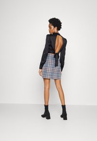 Blusa de cetim preto com costas abertas e detalhe de laço, combinada com uma saia mini em xadrez azul. Modelo usa botas de tornozelo pretas.