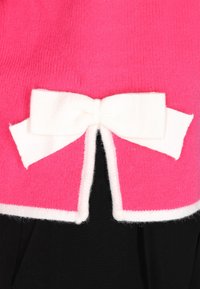 Prenda de punto en color fucsia con un acento en forma de lazo blanco en el dobladillo trasero, con una tela negra contrastante debajo. Textura suave.