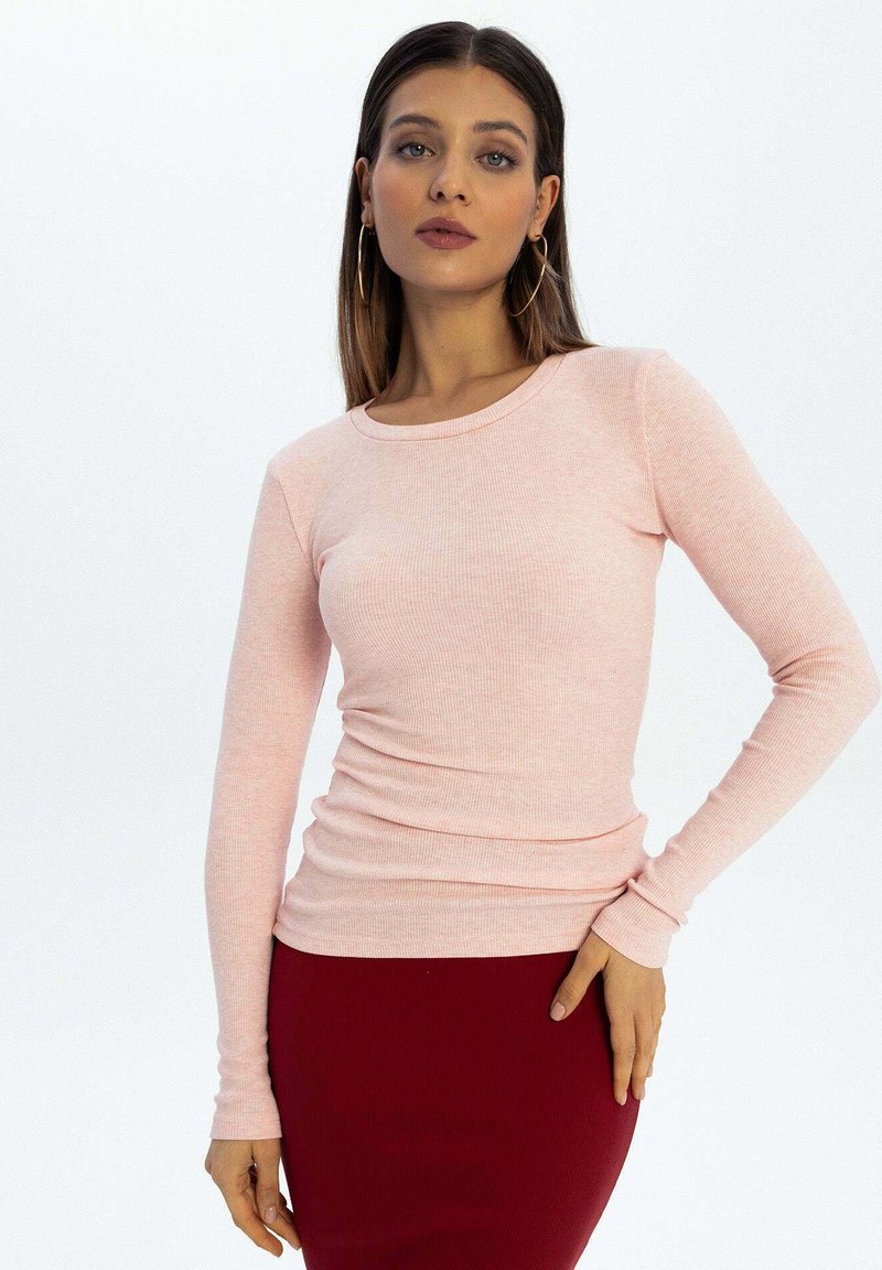 Długi rękaw bluzka w jasnoróżowym kolorze z prążkowanej tkaniny, z okrągłym dekoltem i dopasowanym fasonem, zestawiona z dopasowaną ciemnoczerwoną spódnicą.