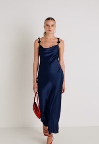Rochie satinată bleumarin cu decolteu tip cowl, bretele subțiri decorate cu accente florale negre și o siluetă lungă, fluidă.