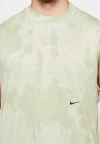 Débardeur de sport vert clair avec motif camouflage subtil et petit logo Nike swoosh noir sur le côté droit.